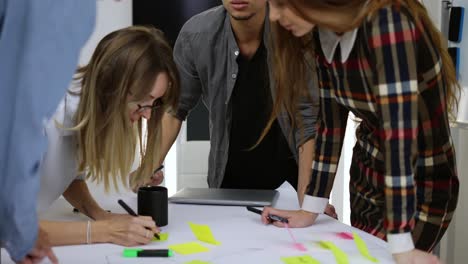 Young-men-and-women-brainstorming,-writing-down,-sharing-ideas-at-the-office