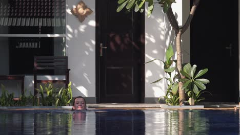 toma amplia de una mujer joven en bikini negro entrando a la piscina de un hotel tropical