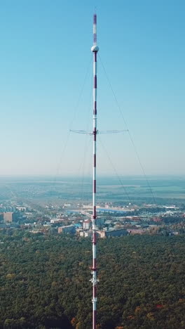 one telecommunication tower is located near the city in the background of the forest. camera motion back vertical video