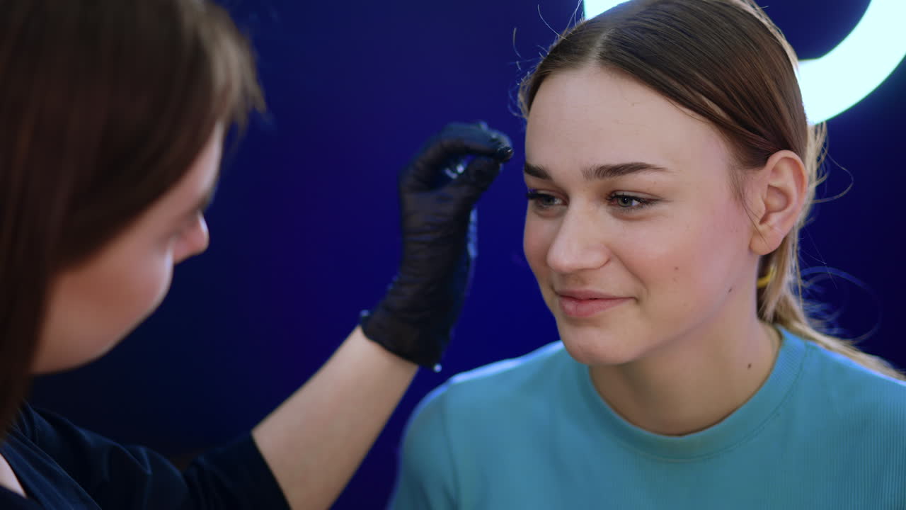 Brow master uses a little brush to comb the eyebrows of a beautiful female client. Beauty procedure in the salon. Close up.
