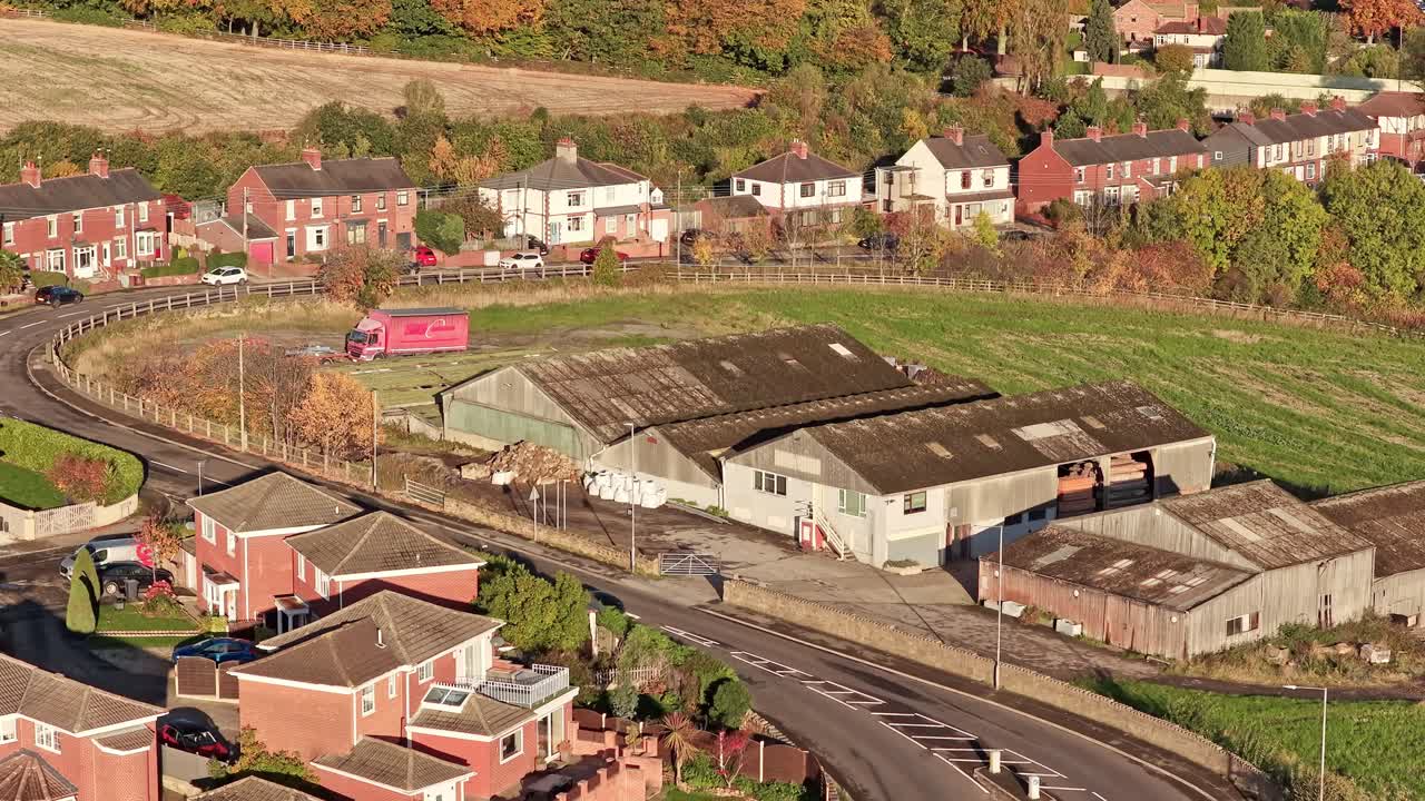 Hemingfield Road in Barnsley, South Yorkshire, showing brick homes, a curved road, and a farm complex surrounded by autumn foliage and open fields drone shots