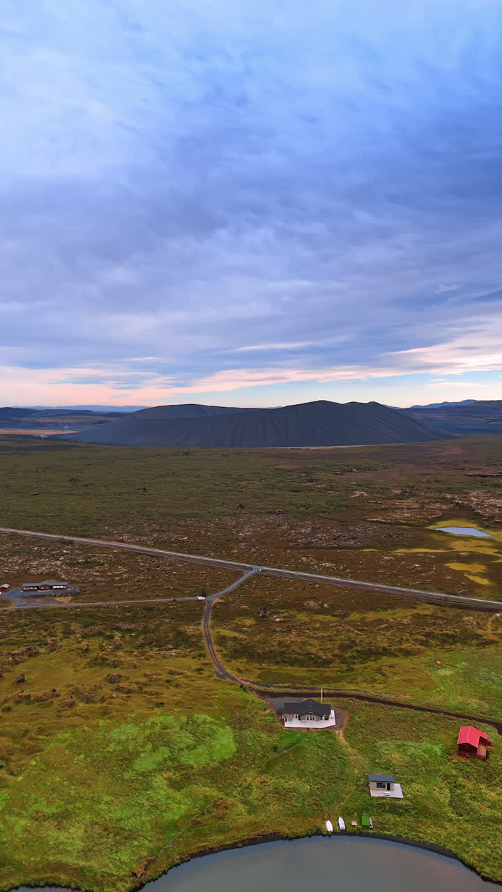 Approaching the waterfront with few lonely houses and road leading to them. Black sleeping volcano at backdrop. Iceland. Vertical video.