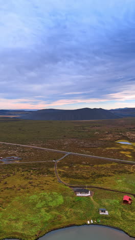 approaching the waterfront with few lonely houses and road leading to them. black sleeping volcano at backdrop. iceland. vertical video.