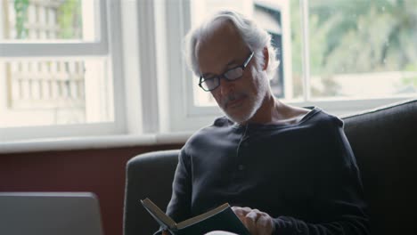 senior man reading a book in living room 4k