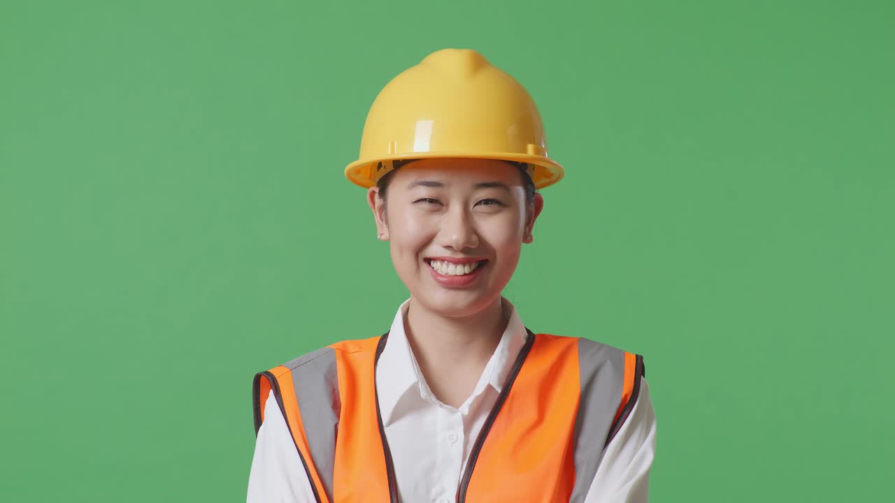 Close Up Of Asian Female Engineer With Safety Helmet Crossing Her Arms And Smiling To Camera While Standing In The Green Screen Background Studio