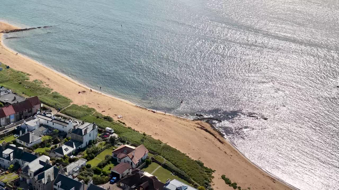 Drone pans above Fife coastline, revealing beach, seaside homes, golf course, and sparkling water