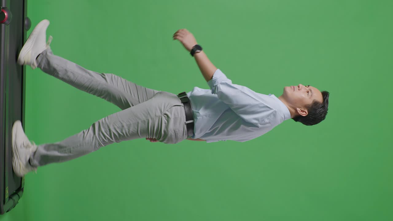 사이드 뷰: 아시아 사업가의 전체 몸체가 걸어서 스튜디오의 녹색 스크린 배경에서 주위를 둘러보고 있습니다.