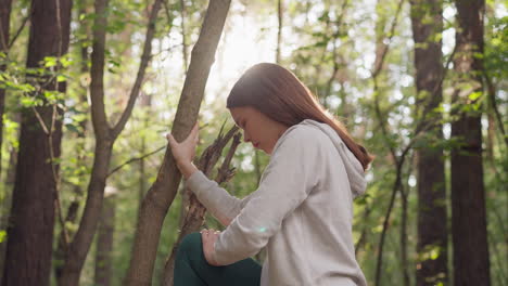 lady stretches leg after run leaning on tree in forest. woman engages in stretching exercises for muscle relaxation as integral part of post-run routine