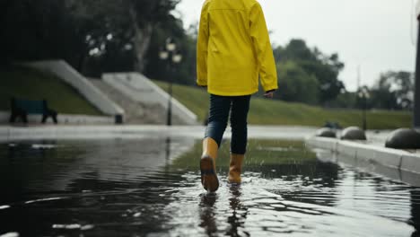 Rückansicht-Eines-Traurigen-Teenager-Mädchens-In-Einer-Gelben-Jacke-Und-Orangefarbenen-Stiefeln,-Das-Nach-Dem-Regen-Die-Straße-Entlang-Läuft