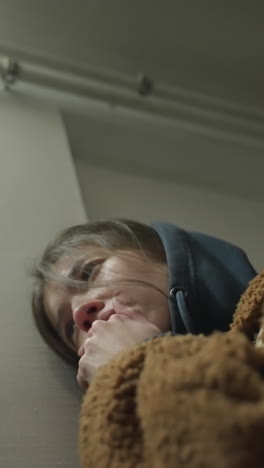 un primer plano de una niña llorona apoyándose en la pared de un túnel subterráneo. ella parece profundamente preocupada, con su mano cubriendo parcialmente su rostro, un momento de angustia emocional