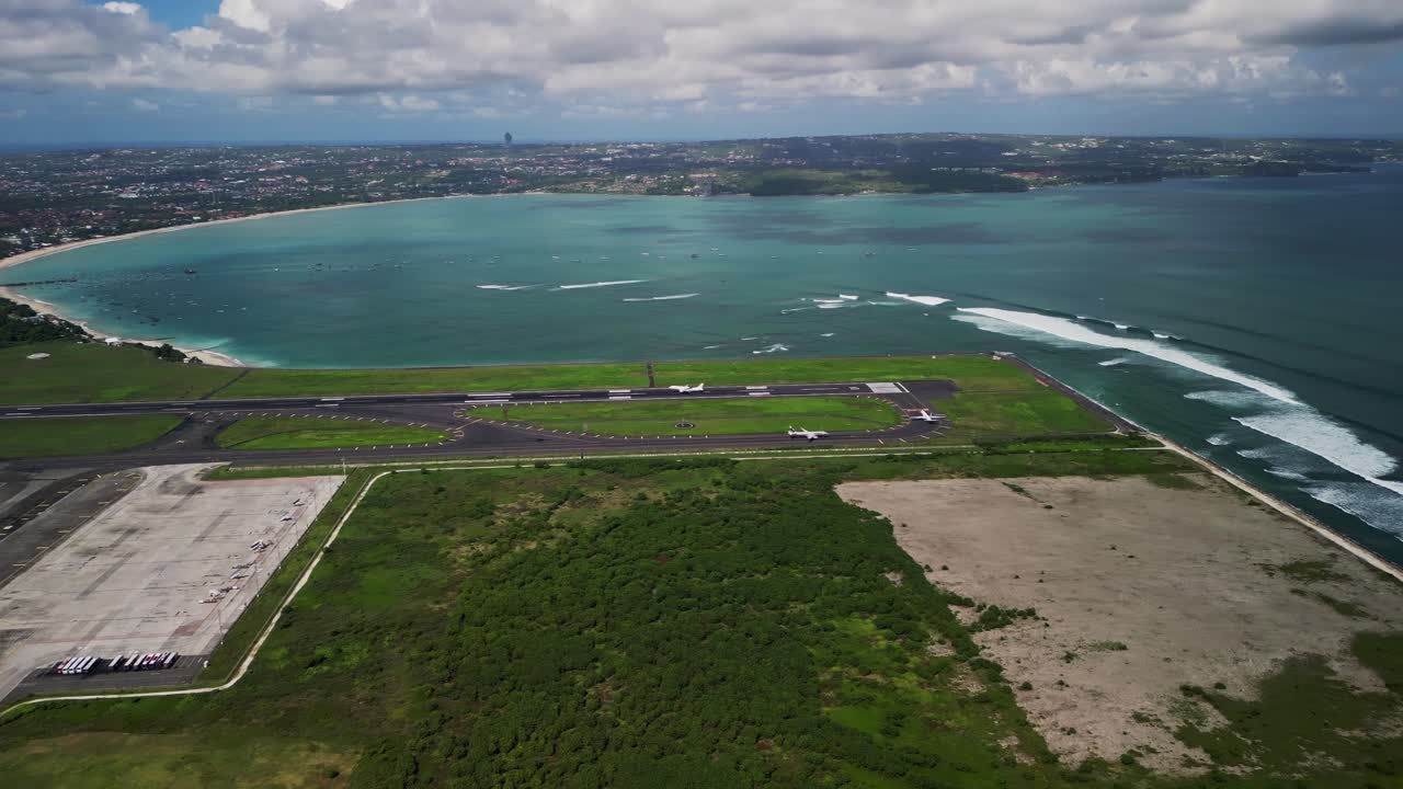 An airplane makes a smooth landing at Bali Airport during daylight hours with views of the runway, nearby ocean, and surrounding tropical landscape.