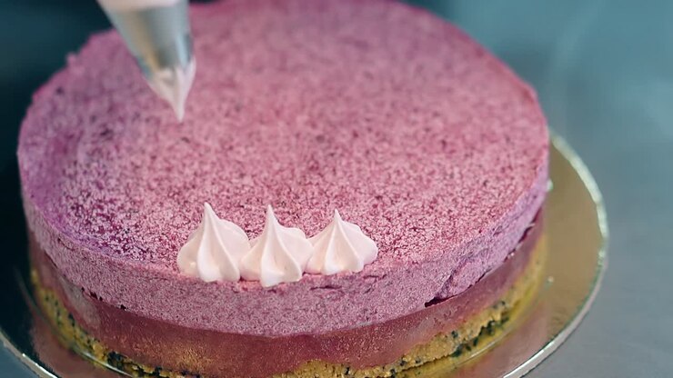 woman gradually decorates pink biscuit cake top with cream