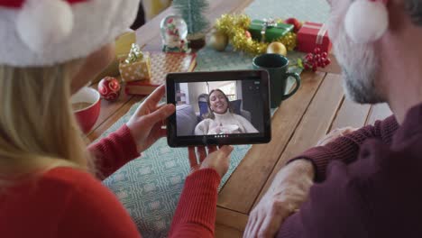 Caucasian-couple-with-santa-hats-using-tablet-for-christmas-video-call-with-woman-on-screen