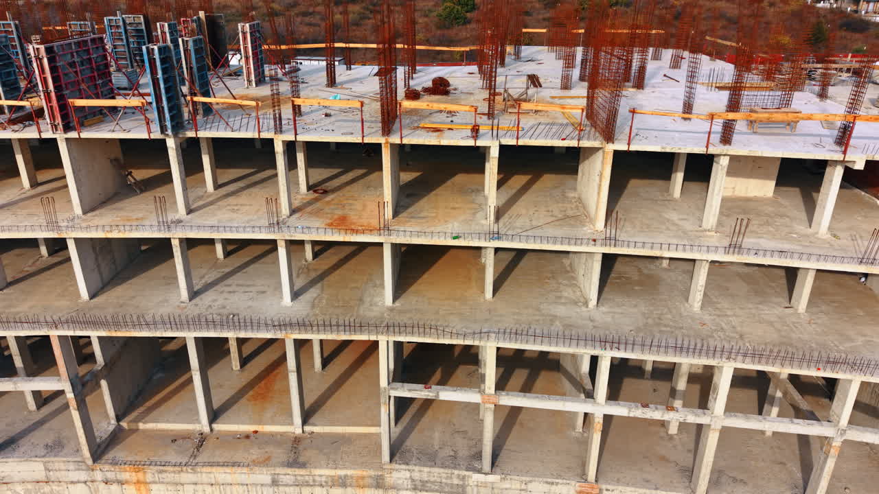 Frame of the large multi-storied building. Metal rebars stick on the top. Drone footage above the future hotel
