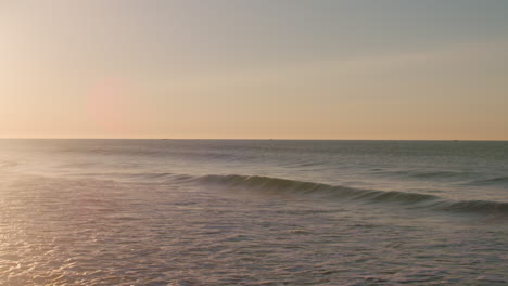 Small-waves-breaking-during-a-calm-sunrise-in-Luz,-Portugal