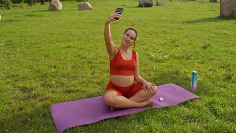 mujer embarazada tomando una selfie mientras hace yoga al aire libre