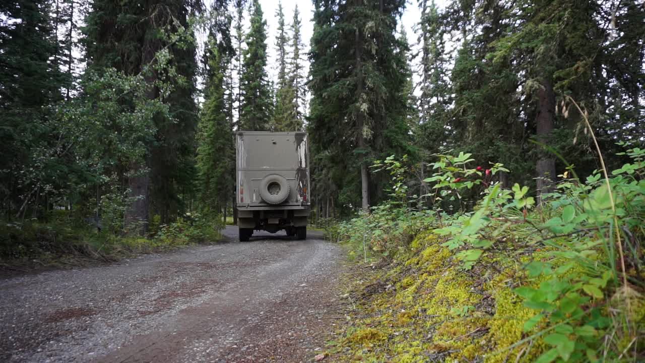 알래스카주 이글 근처의 가문비나무 숲을 가로질러 운전하는 대형 오프로드 트럭의 정적인 낮은 앵글 샷