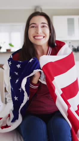 vertical video of happy caucasian woman with flag of usa watching tv