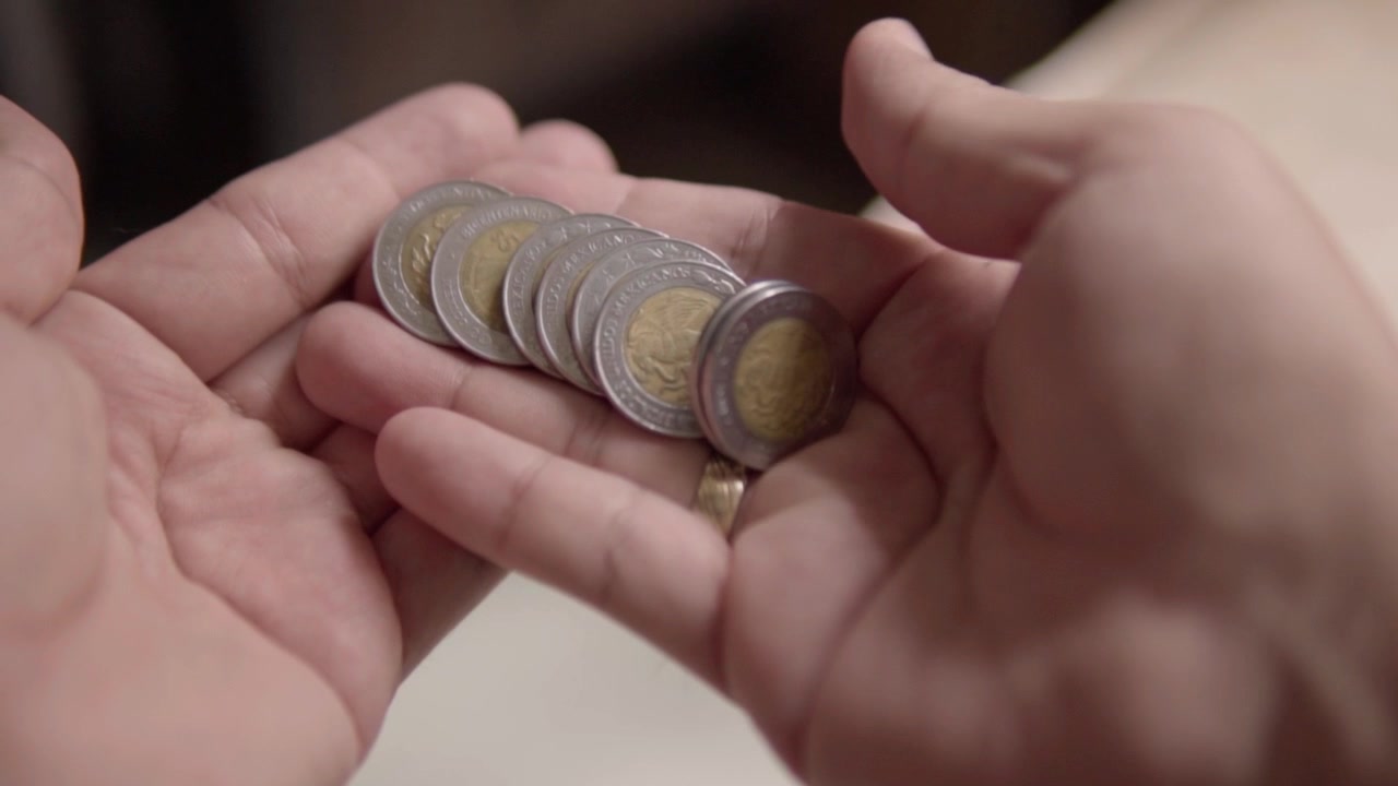Primo piano di mani che contano monete messicane impilate, maneggiando valuta metallica per pagamenti in contanti o transazioni finanziarie in Messico durante la gestione quotidiana del denaro