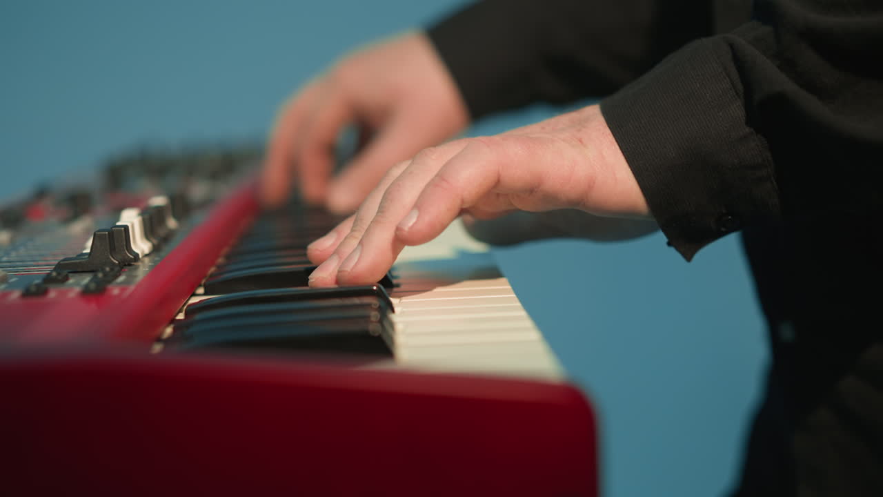 tecladista sin rostro tocando un piano sampler rojo contra un fondo azul. el primer plano hace hincapié en las manos del músico en las teclas mientras la cámara hace zoom