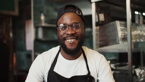 Portrait-of-a-Black-person-in-a-doner-market.-Man-with-glasses-posing-and-smiling