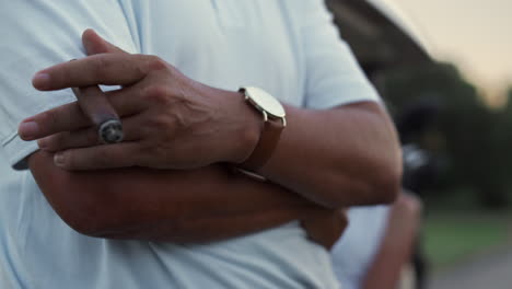 un hombre fumando un cigarro a mano junto a un carrito de golf. una pareja rica disfruta descansando en un coche de golf.