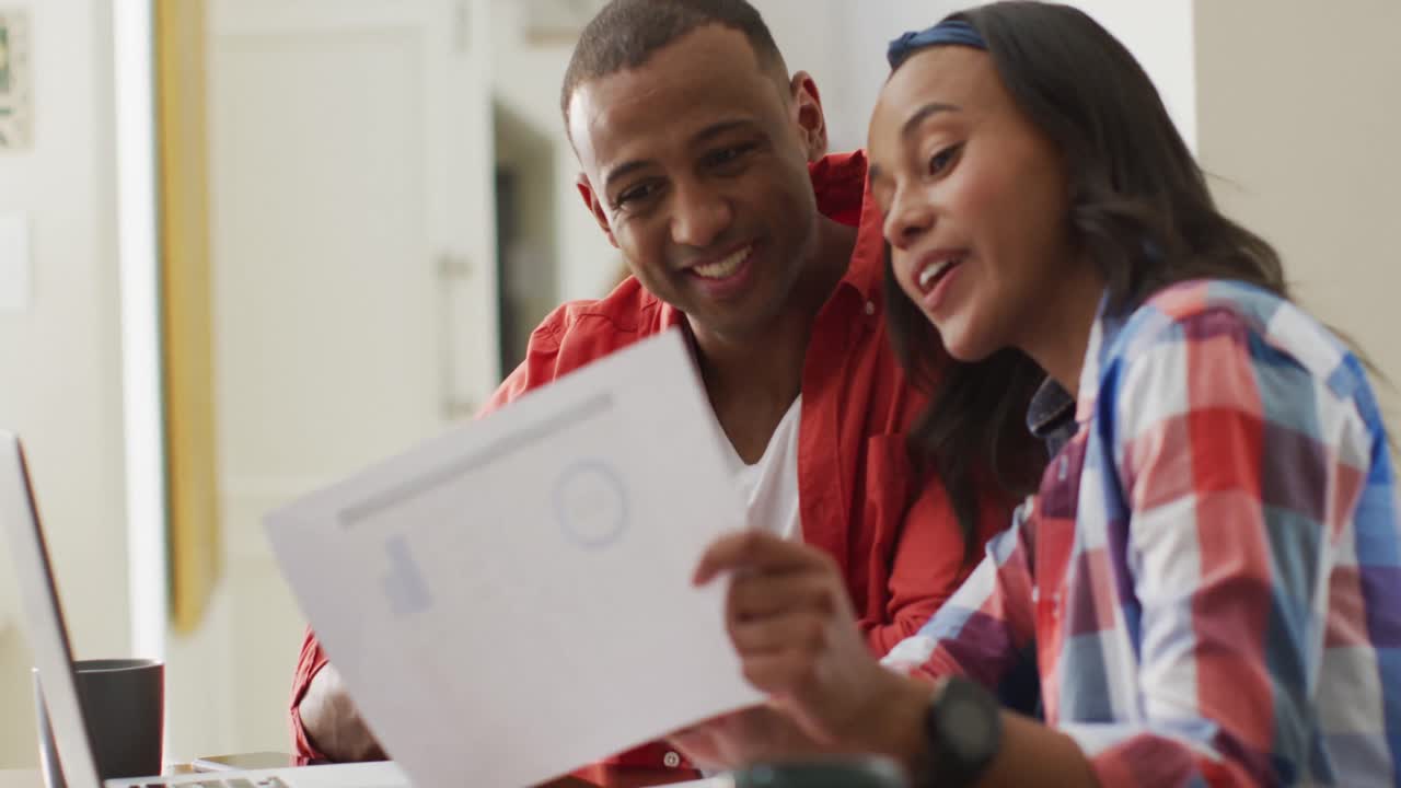 Happy biracial couple sitting at table with laptop and counting home budget