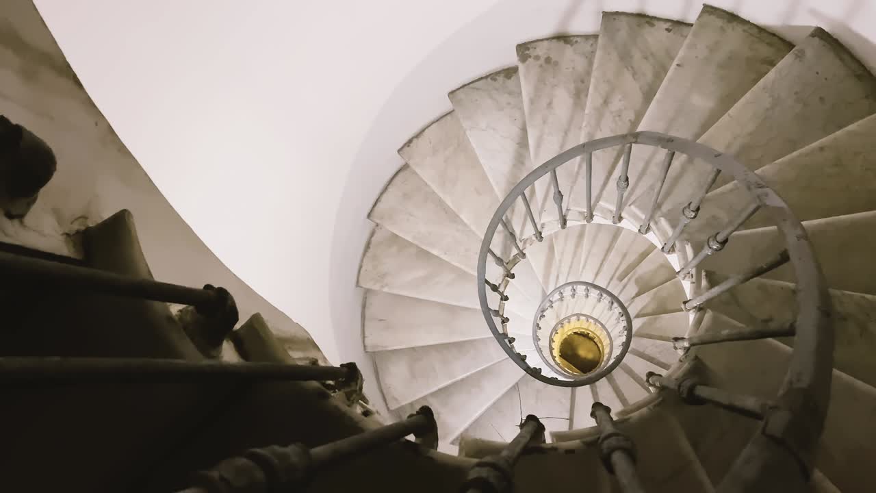 mirando desde la parte superior de una antigua escalera en espiral con barandillas de hierro y escalones de mármol
