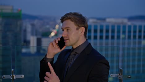 happy caucasian businessman talking on phone on rooftop terrace at sunset with city skyline in the background