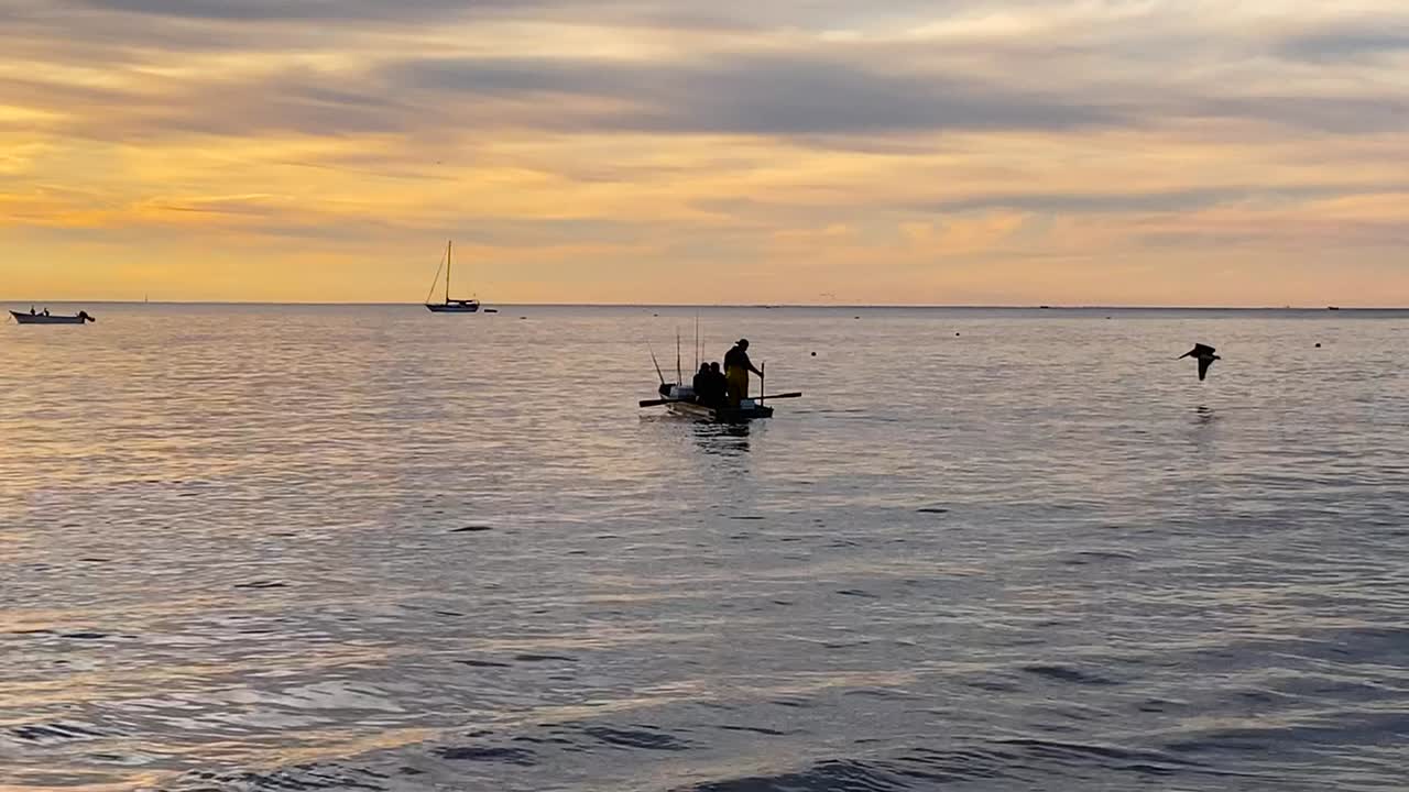 Shot of a group fishermen rowing boat against outgoing tide to catch fish at Bahia Asuncion, Mexico at sunrise