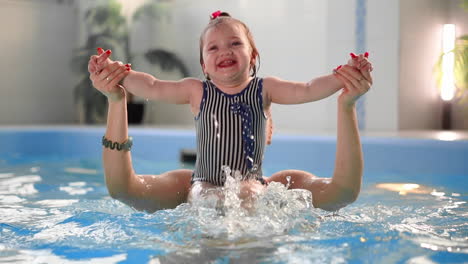 cute blonde toddler in protective glasses is diving under the water together with his mother in the swimming pool trying to take out his toy. his mother is teaching him how to swim. an underwater shot.