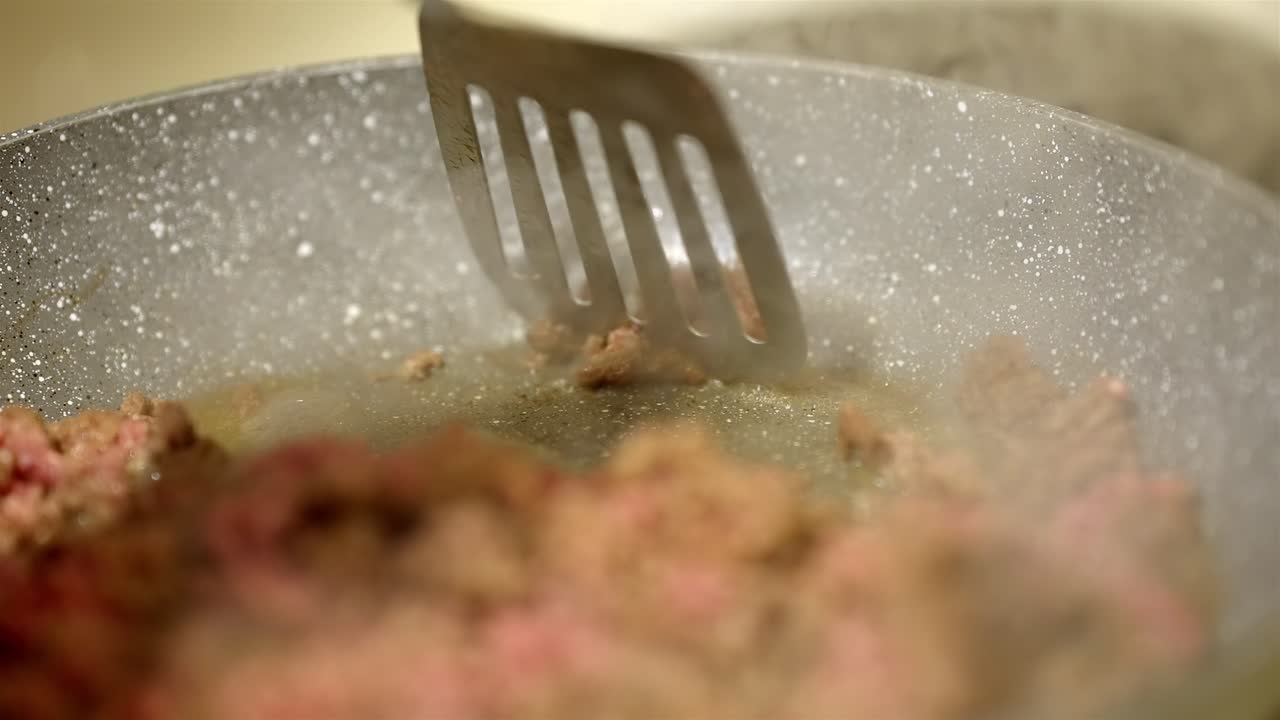 Cooking ground beef in frying pan with steam rising, close up view