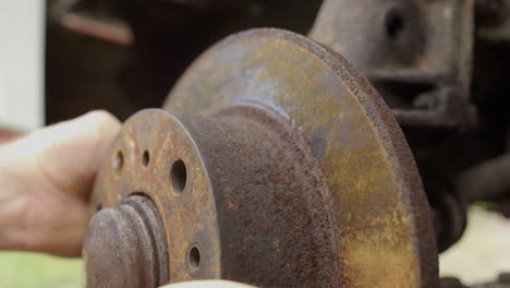 Close-up-side-view-of-caucasian-hands-removing-rusty-disc-brakes-from-car-axle