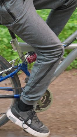 vista lateral de un ciclista montando a lo largo de un camino sin asfalto rodeado de exuberante vegetación, el ciclista lleva pantalones y zapatillas grises mientras disfruta de un paseo tranquilo en la naturaleza