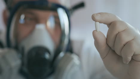 close up in the laboratory a man in a glass respirator screen holding a new medicine a white pill an antibiotic against the virus and looking at it. high quality 4k footage