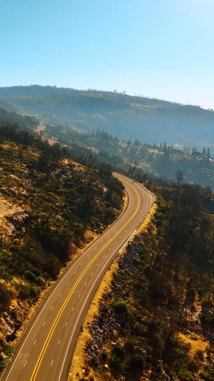 Flying above the sunlit highway in the mountains. Sunny day footage in Sierra National Forest, California, USA. Vertical video
