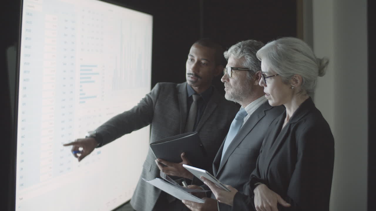 Confident professional finance people with documents and screen with data