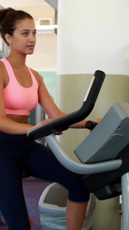 vertical video of fit brunette working out on the exercise bike at the gym