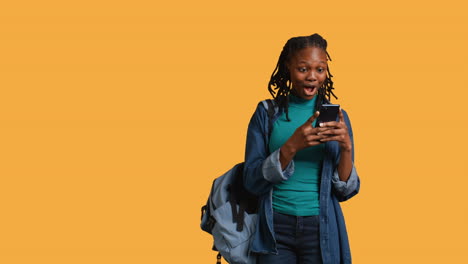 Portrait-of-overjoyed-teenager-reading-messages-on-phone,-studio-background