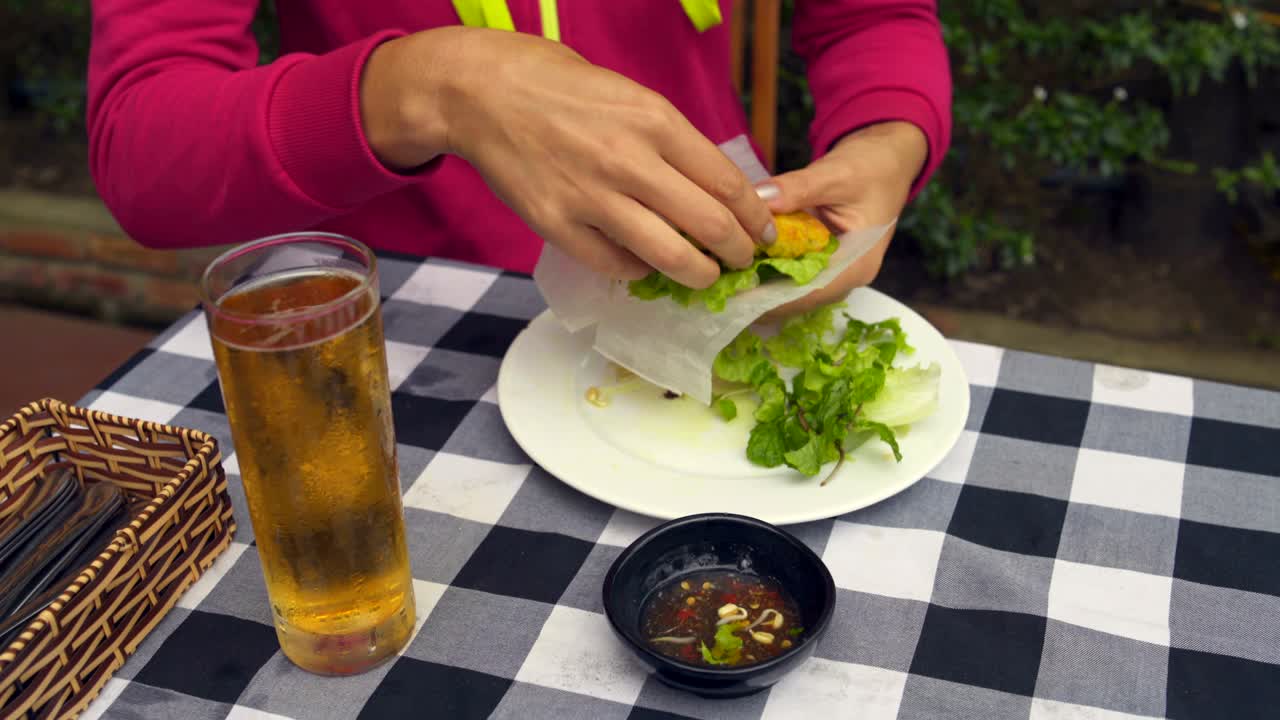 una mujer hace un rollo vegetariano de papel de arroz, verduras y tortilla