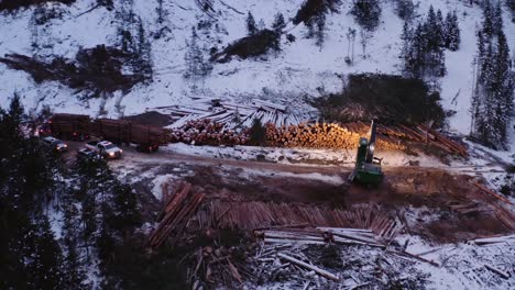 drone pulling away backwards from industrial timber manipulator in operation while wood loaded truck pulls away