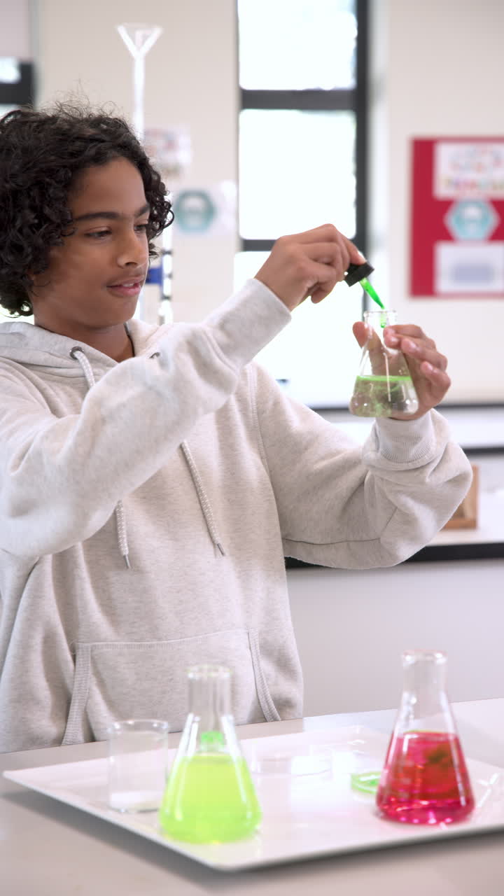 Vertical video: Student in science class experimenting with colorful liquids in laboratory flask