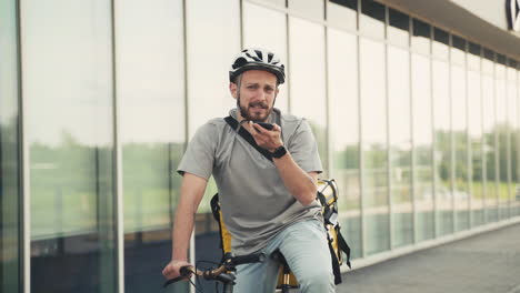 happy food delivery man wearing thermal backpack on his bicycle sending an audio message with his smartphone