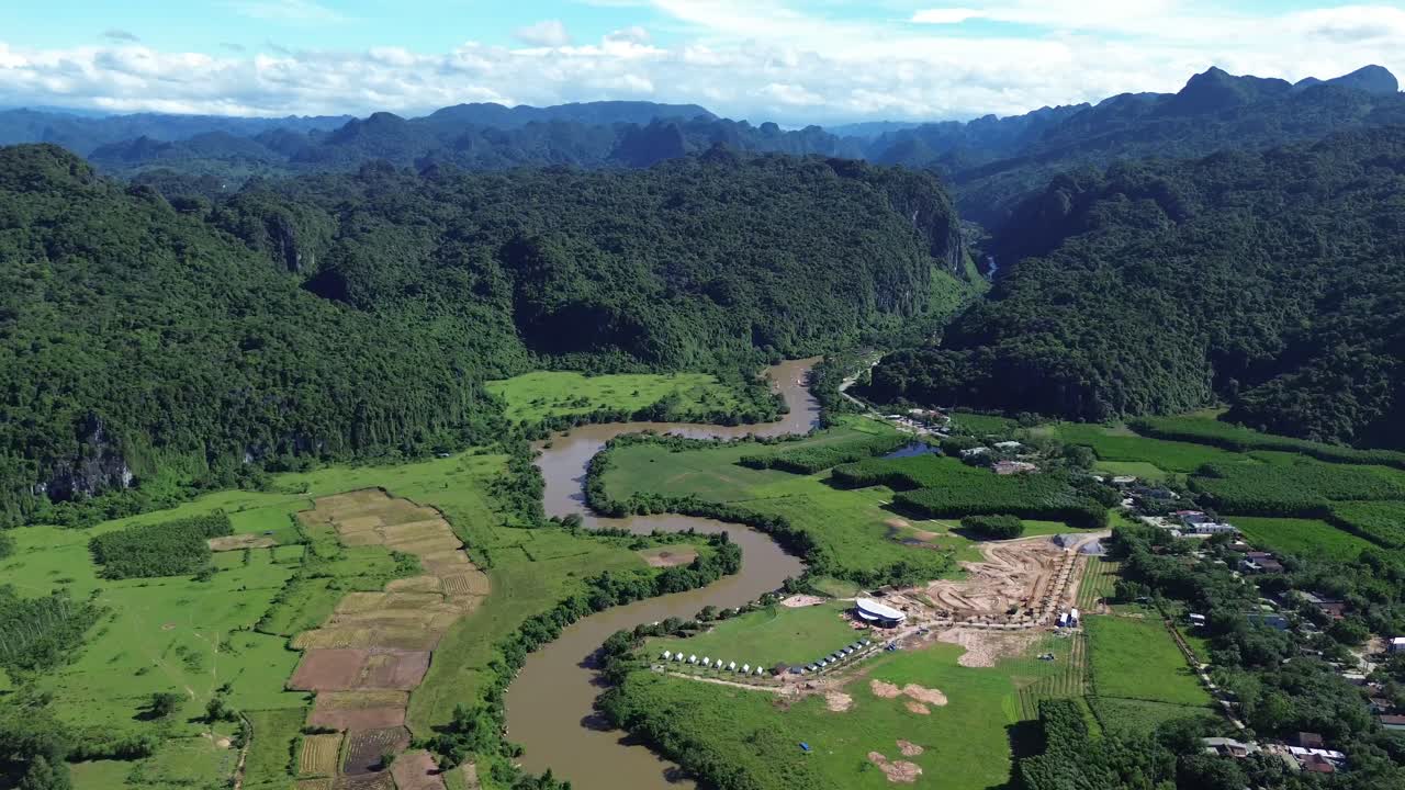 Drone pan right showing winding muddy river cutting through green farmland and forested karst landscape