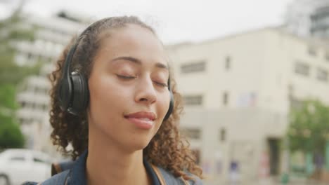 happy biracial woman in city, wearing headphones and smiling