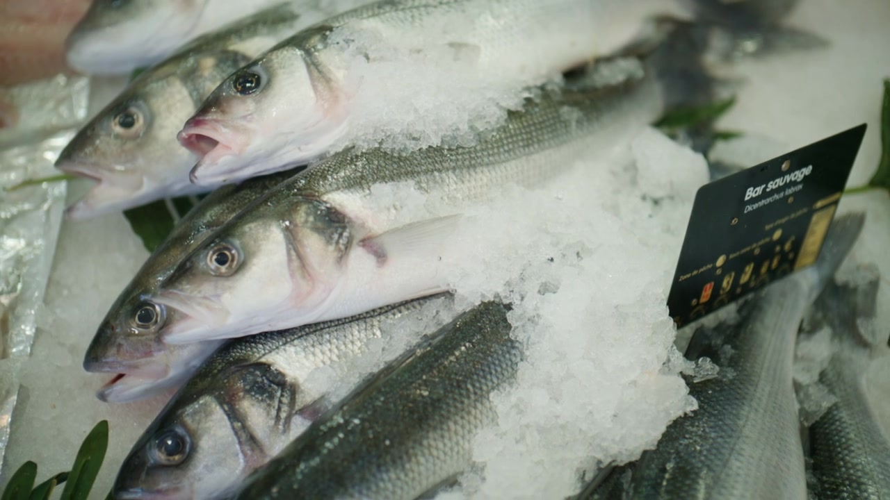 Close-up de peixe prateado fresco exposto em gelo picado em um mercado de frutos do mar.