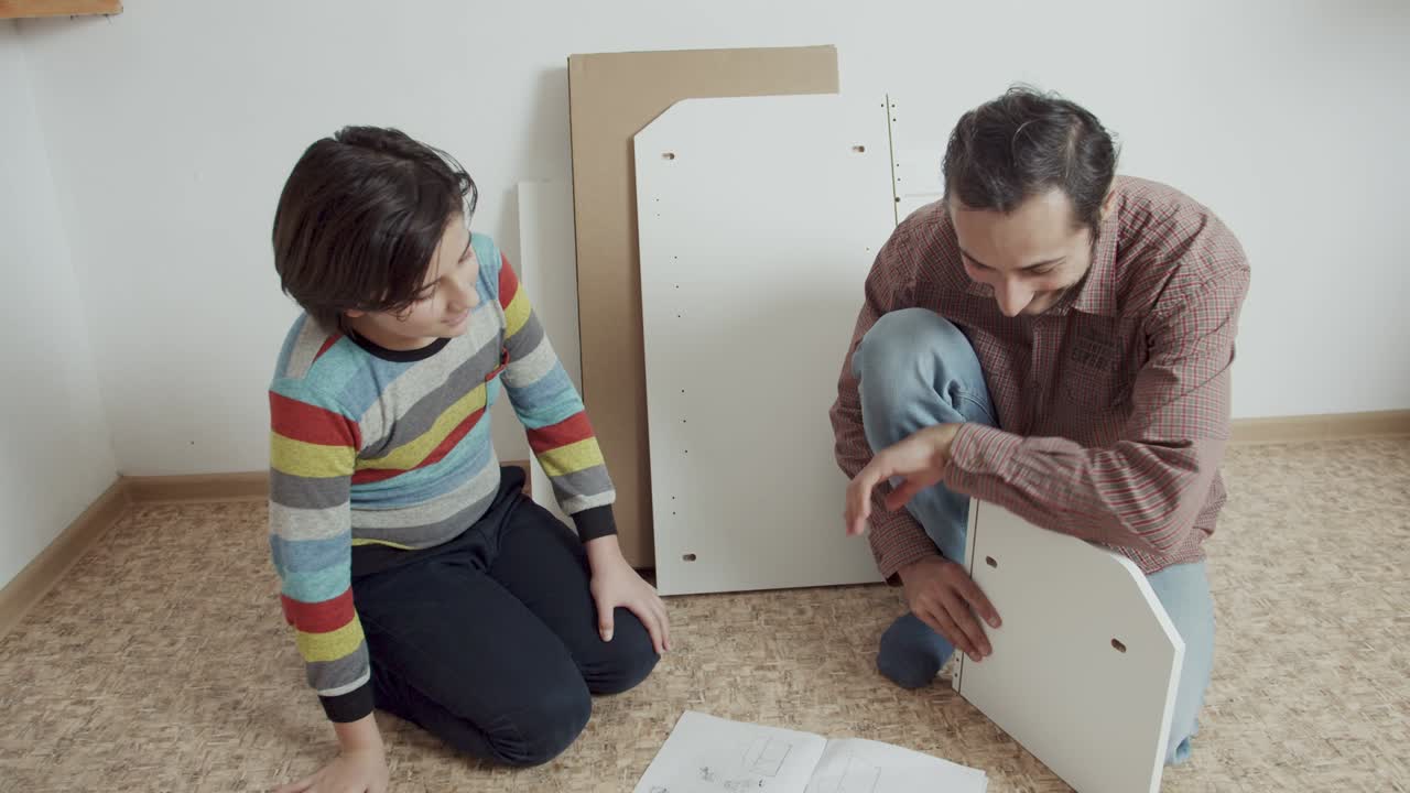 padre e hijo montan muebles de acuerdo con las instrucciones en el suelo de la habitación. ayudan con la tarea. ahorran el presupuesto familiar
