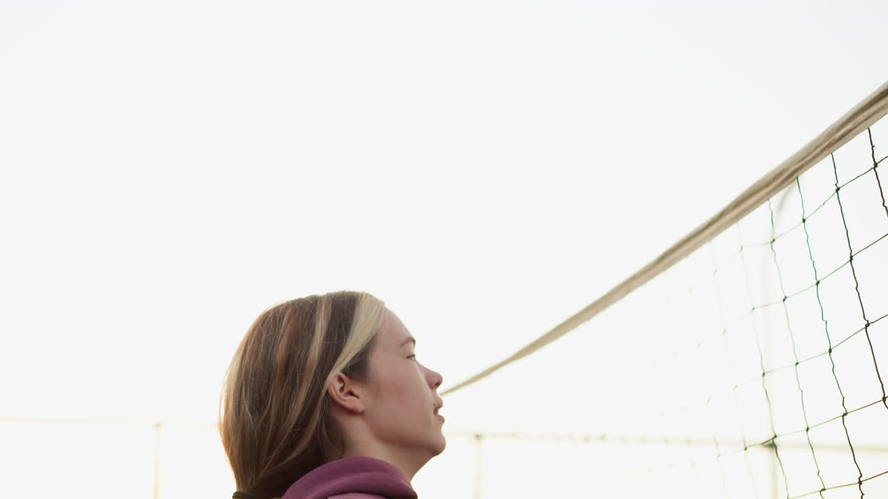 배구 선수가 전체 초점을 맞추고 슬램 볼로 점프하는 측면 뷰, 배경에 볼 수 있는 배구 네트, 강렬한 순간 동안 힘과 결단력을 보여주는 운동 선수