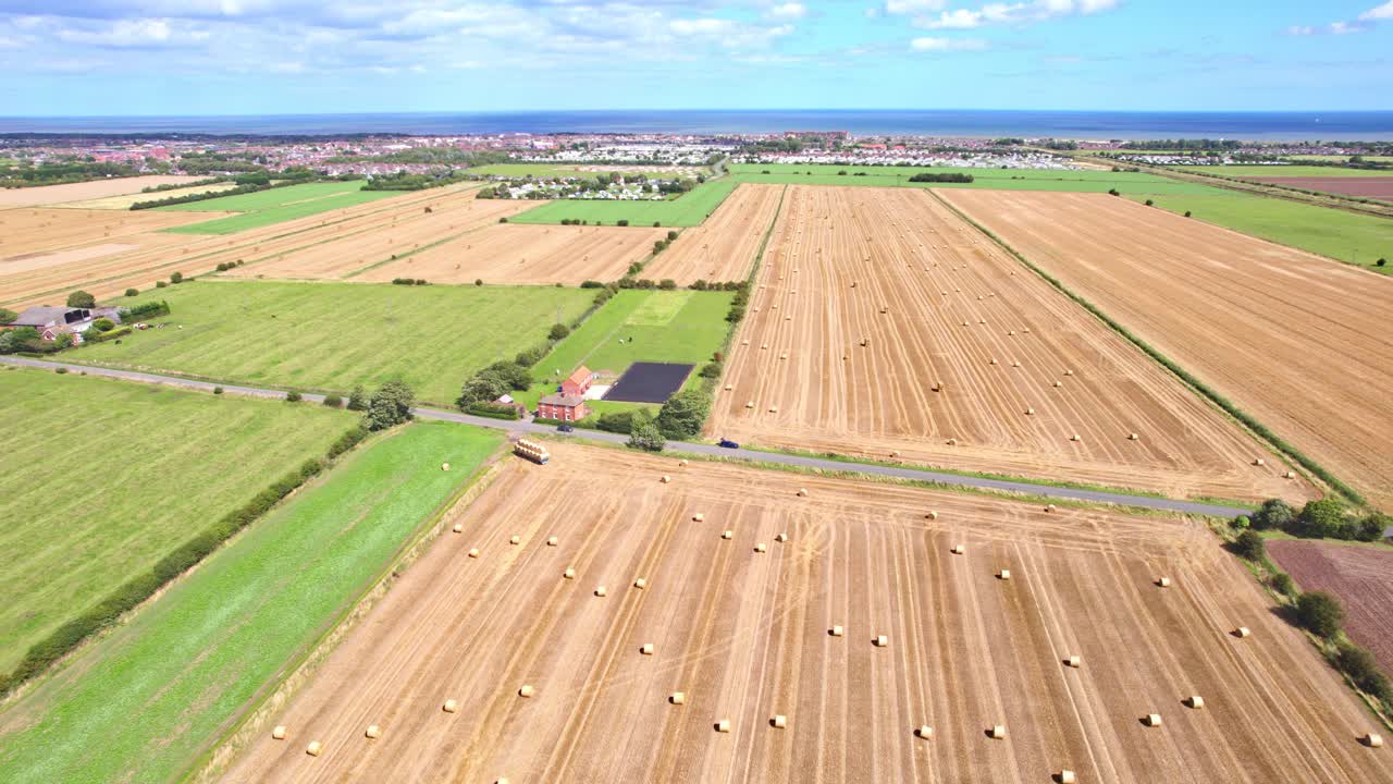 Captured from above, a video showcases a line of wind turbines gracefully spinning amidst a recently harvested field in Lincolnshire, with golden hay bales in the foreground