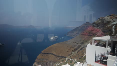 Beautiful-Wide-Shot-of-The-View-From-The-City-of-Thira-in-Santorini-Greece-in-a-Restaurant-With-Cliffs,-People,-Boats-and-Islands-in-the-Background